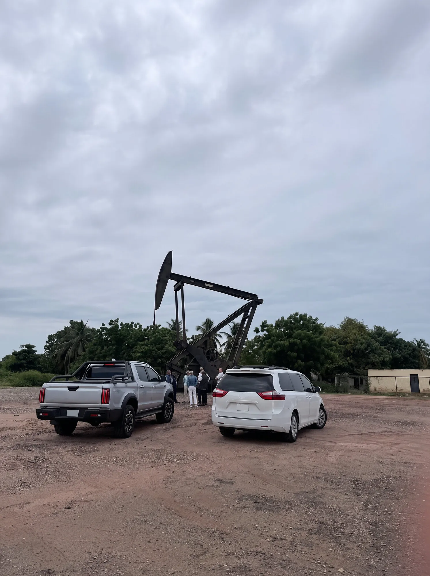Una pickup y una minivan junto a un balancín de extracción petrolera