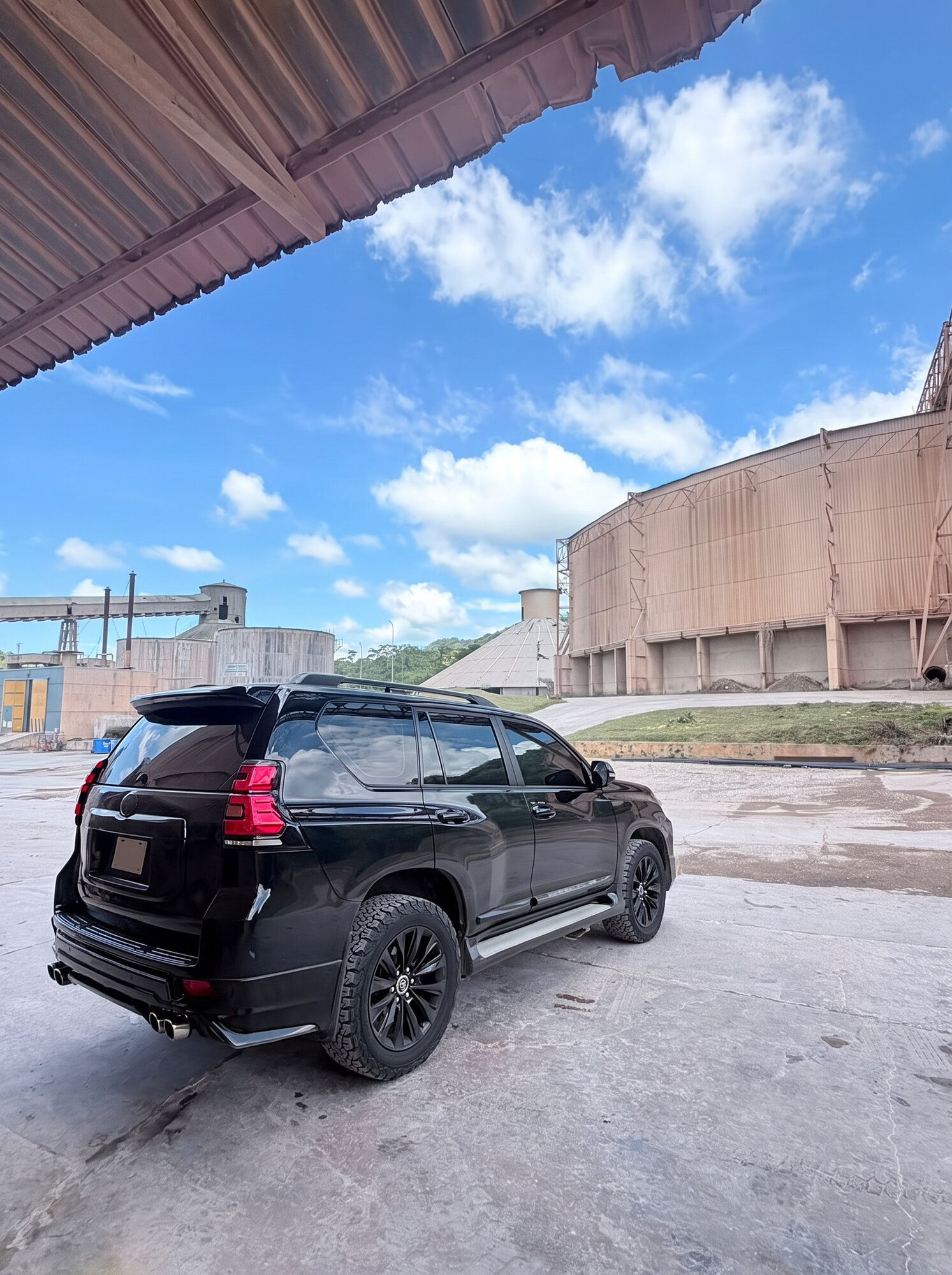 Camioneta negra estacionada frente a los silos de una planta industrial