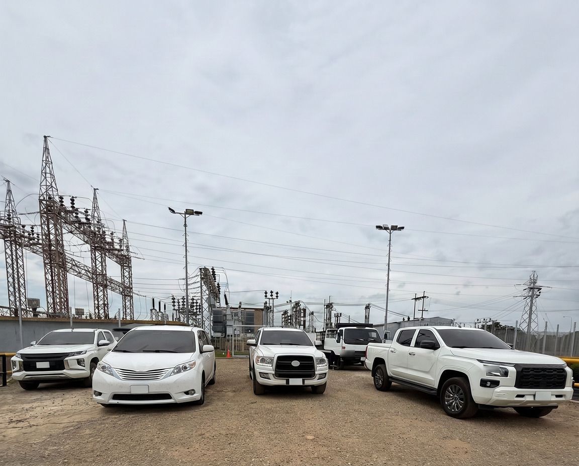 Cinco vehículos blancos estacionados frente a las torres de una subestación eléctrica